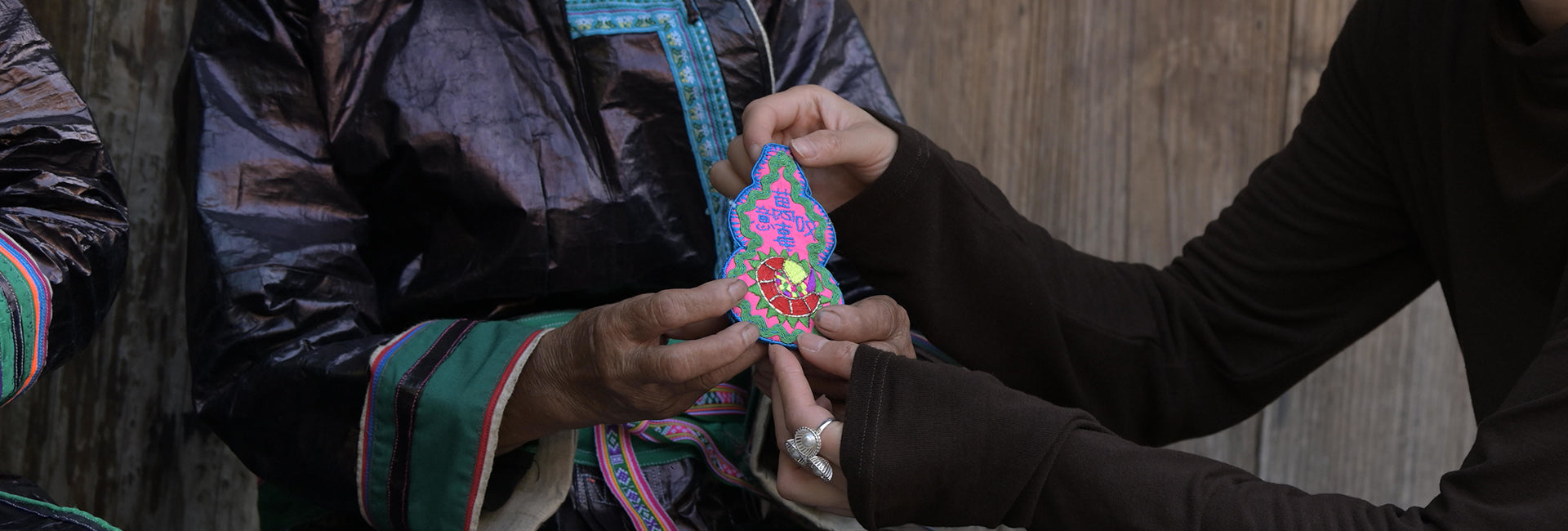 Dong elder passing a gourd-patterned fabric to a young woman